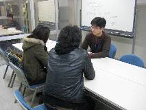 数学・物理学習支援室で学生(後ろ姿の2人)の質問に親身に答える教員スタッフの写真